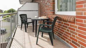 A balcony with a table and chairs, a window with a view, and a brick wall. - Apartment Aurelia - Apartments in the North Sea Garden Park (Esens)