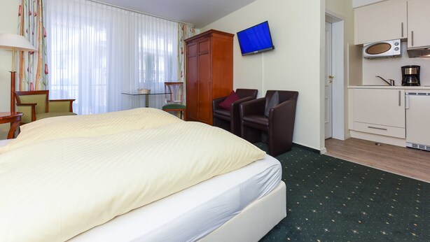 A hotel room with a bed, a television, a desk, a chair, and a kitchenette. - Apartment Aurelia - Apartments in the North Sea Garden Park (Esens)