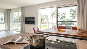 A modern kitchen with a large window, a dining area with a wooden table, and a TV mounted on the wall.