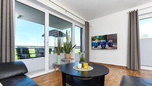 A modern living room with a black sofa, a round black table, and a potted plant. - Apartment Buhne 6 - Residence Waterkant (Esens)