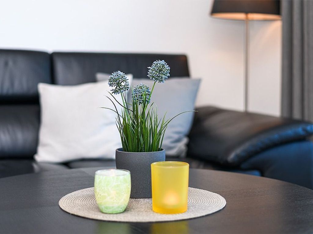 Ein modernes Wohnzimmer mit einem dunklen Sofa, einer kleinen Topfpflanze und zwei Kerzen auf einem runden Tisch.