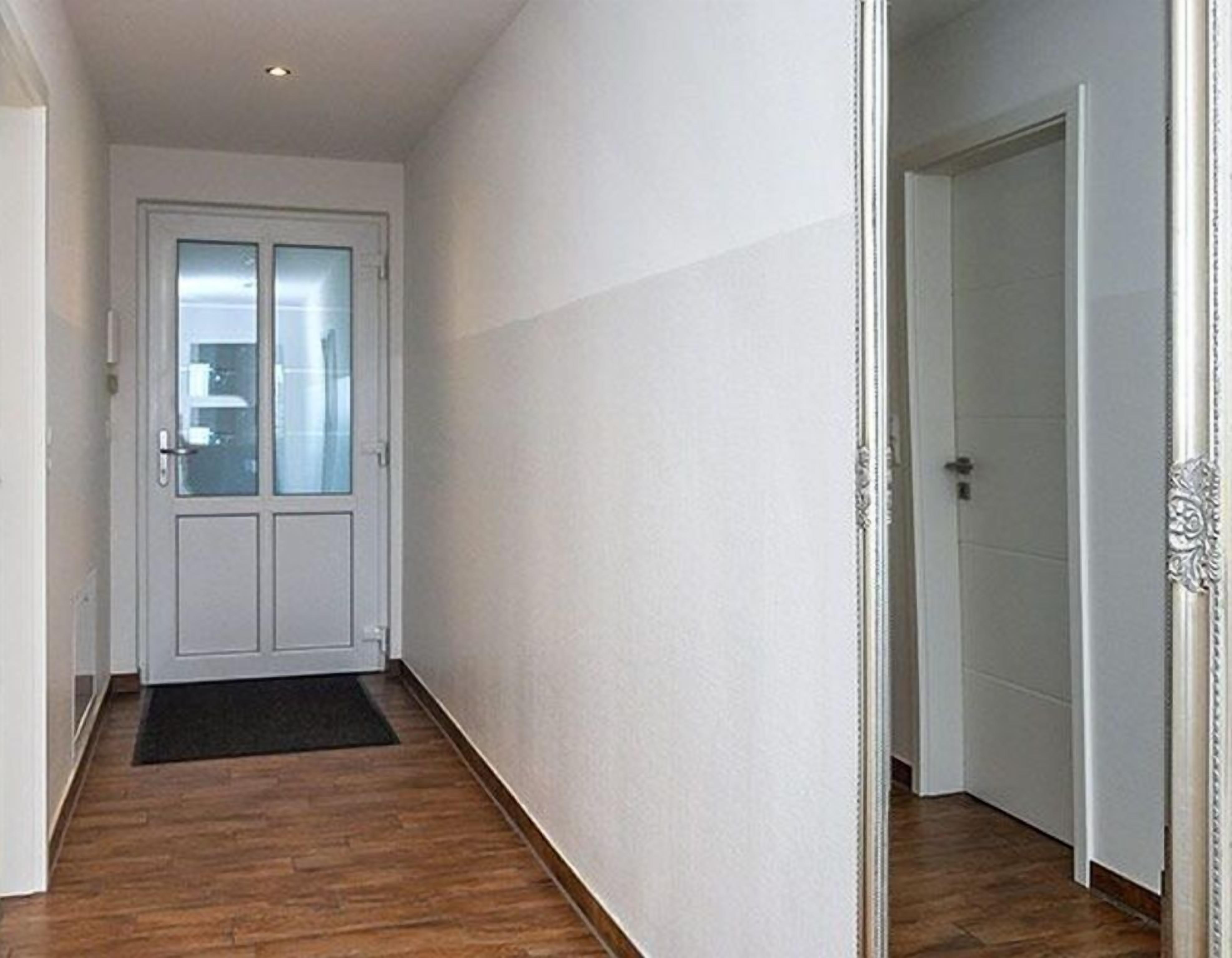 Un couloir doté d’un plancher en bois, de murs blancs et d’une porte avec un panneau de verre.