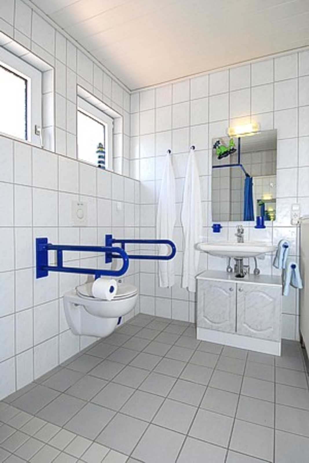 A bathroom with white tiled walls, a toilet, a sink, and a mirror.