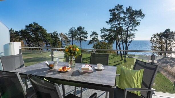 Una terraza con una mesa preparada para dos, con vistas a un cuerpo de agua y un campo de golf.