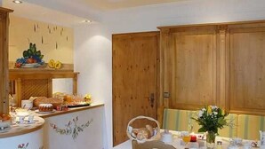 Un coin repas avec une table dressée pour deux personnes, un buffet en bois et un comptoir où sont disposés des produits alimentaires.