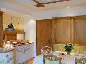 Un coin repas avec une table dressée pour deux personnes, un buffet en bois et un comptoir où sont disposés des produits alimentaires.