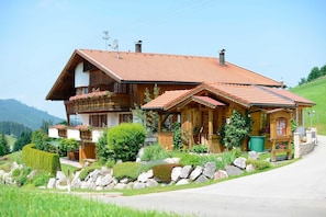 A wooden chalet with a sloped roof, a balcony with flower boxes, and a stone pathway leading to the entrance.