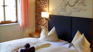 Une chambre d’hôtel avec deux lits, une tête de lit, une table de chevet, une lampe, une fenêtre avec des rideaux et un mur orné d’un tableau décoratif.