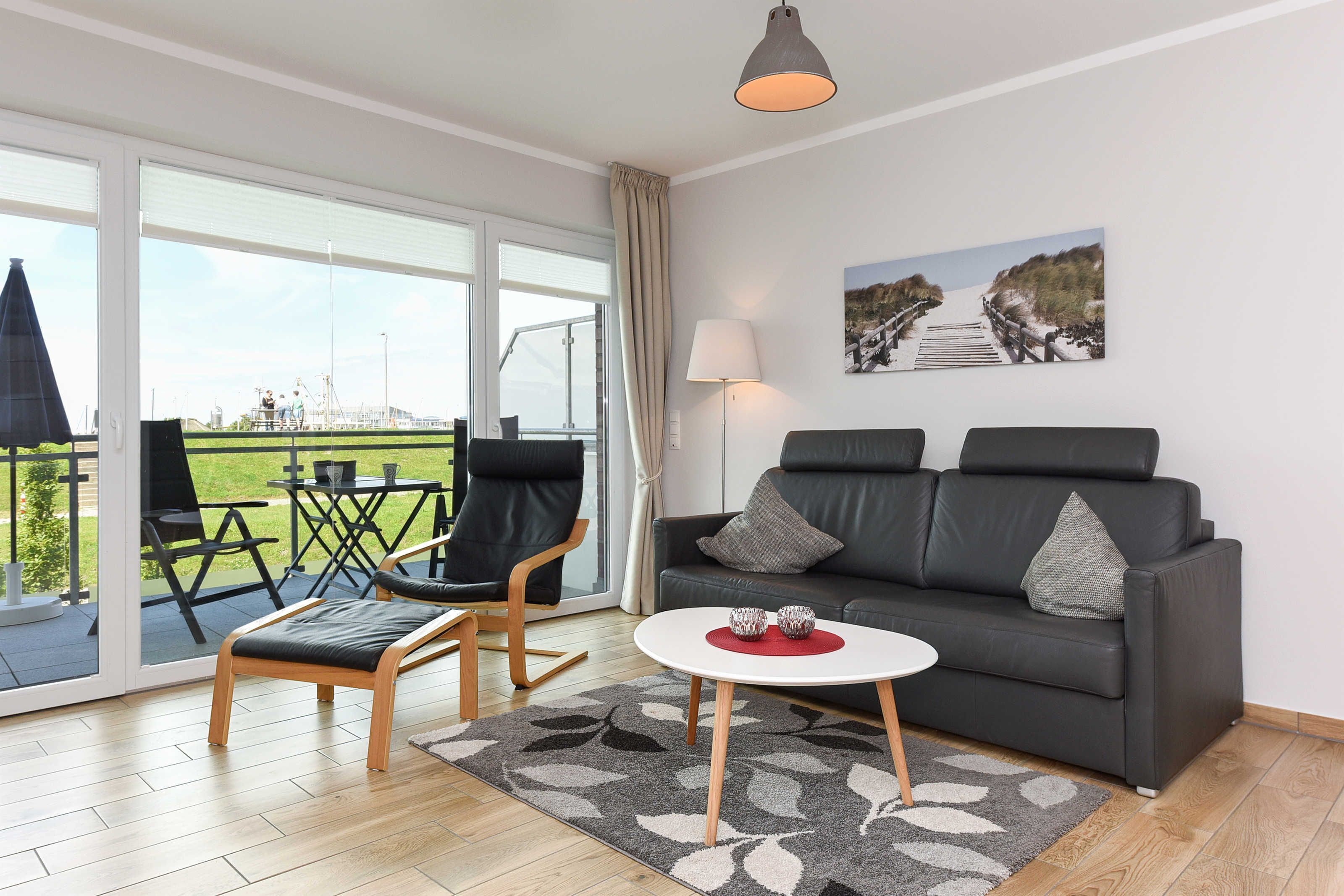 A modern living room with a grey sofa, two black armchairs, a white coffee table, and a large window offering a view of a green landscape.