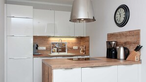 Una cucina moderna con mobili bianchi, un piano di lavoro in legno, un lampadario e una macchina da caffè, con un orologio appeso al muro.