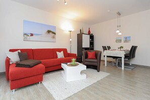 Ein modernes Wohnzimmer mit einem roten Sofa, einem weißen Couchtisch und einem Essbereich mit Tisch und Stühlen.