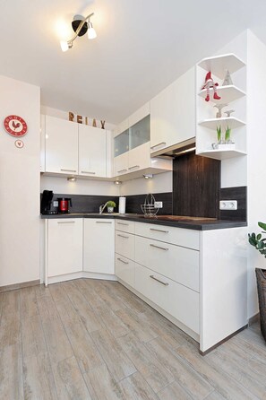 Eine moderne Küche mit weißen Schränken, einer schwarzen Arbeitsplatte und einem dekorativen Regal mit Pflanzen.