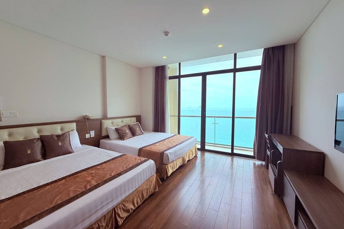 Een hotelkamer met twee bedden, een groot raam met uitzicht op zee en een flatscreen televisie.