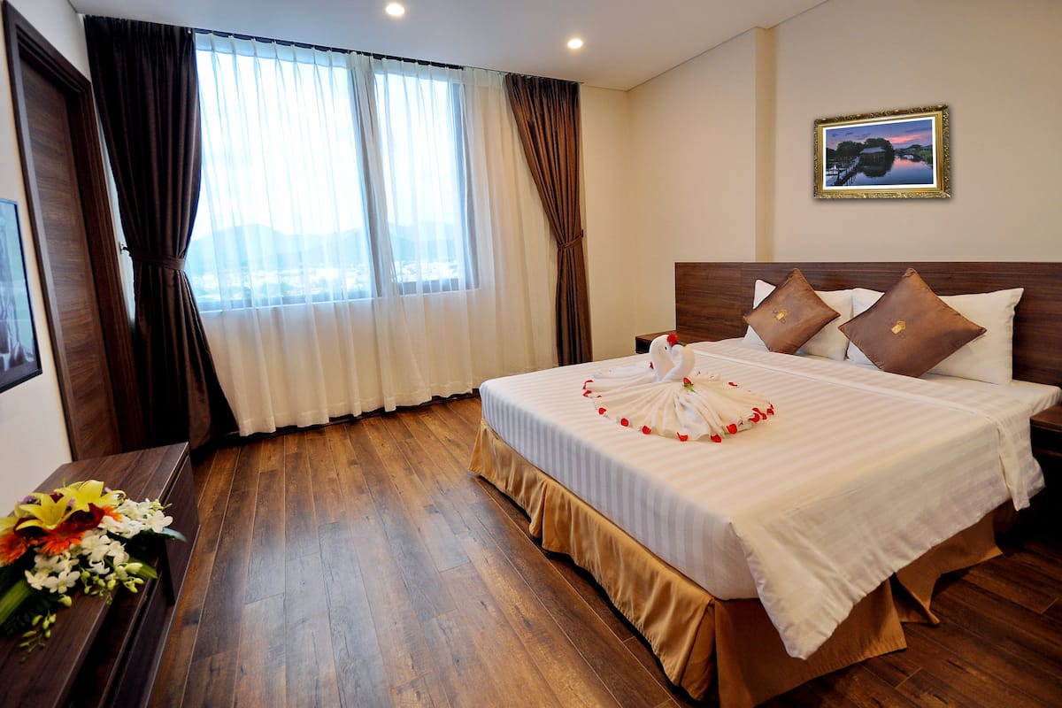 Een hotelkamer met een groot bed, houten vloer en uitzicht op de stad door het raam.