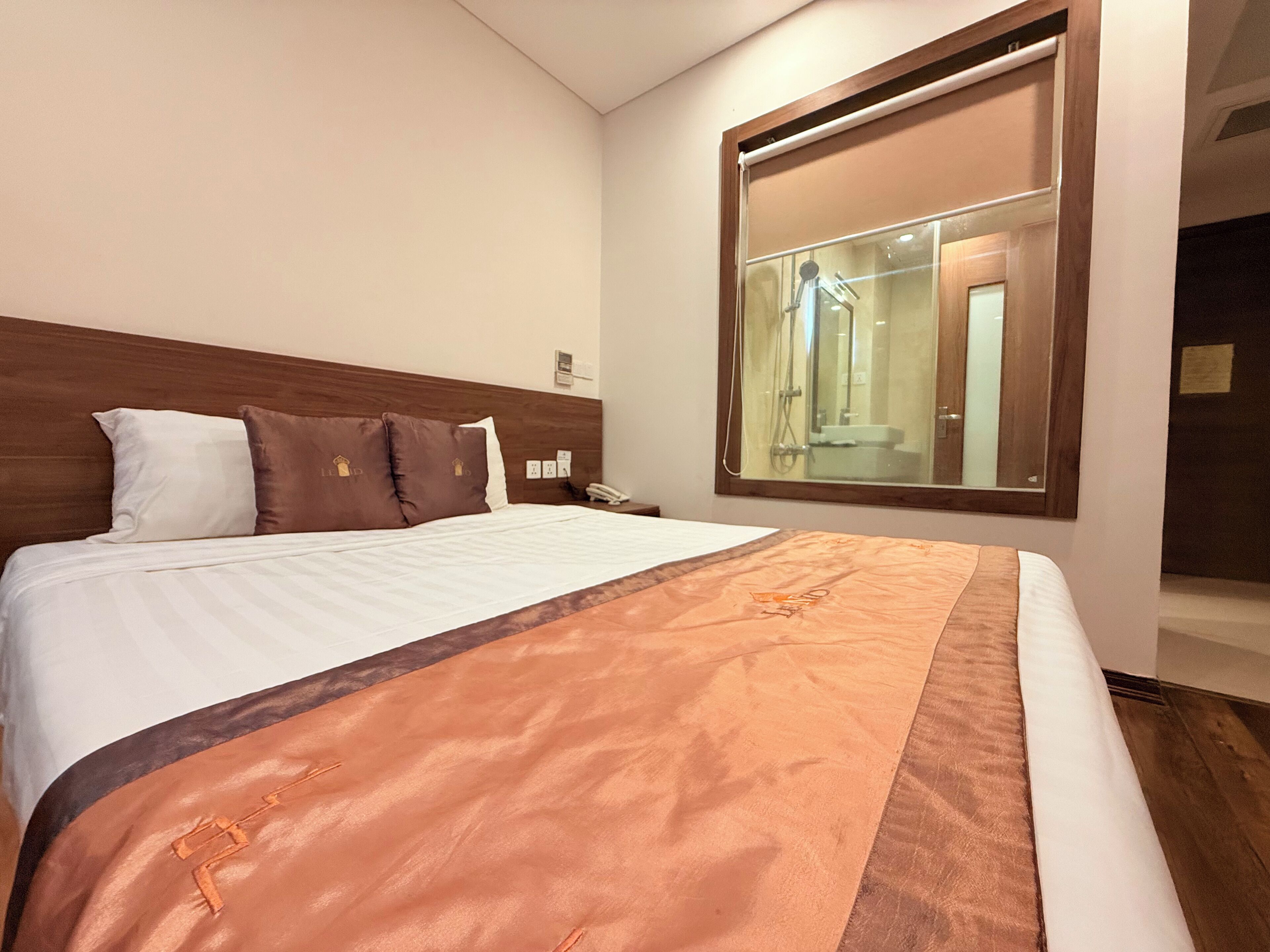 A hotel room with a large bed, a wooden headboard, a mirror, and a view of the bathroom.