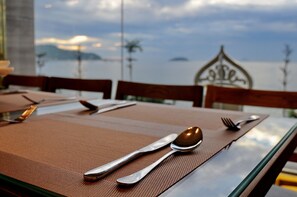 A dining table set with cutlery and a placemat, overlooking a scenic view of the sea and mountains. - Lenid Nha Trang Hotel (Nha Trang)
