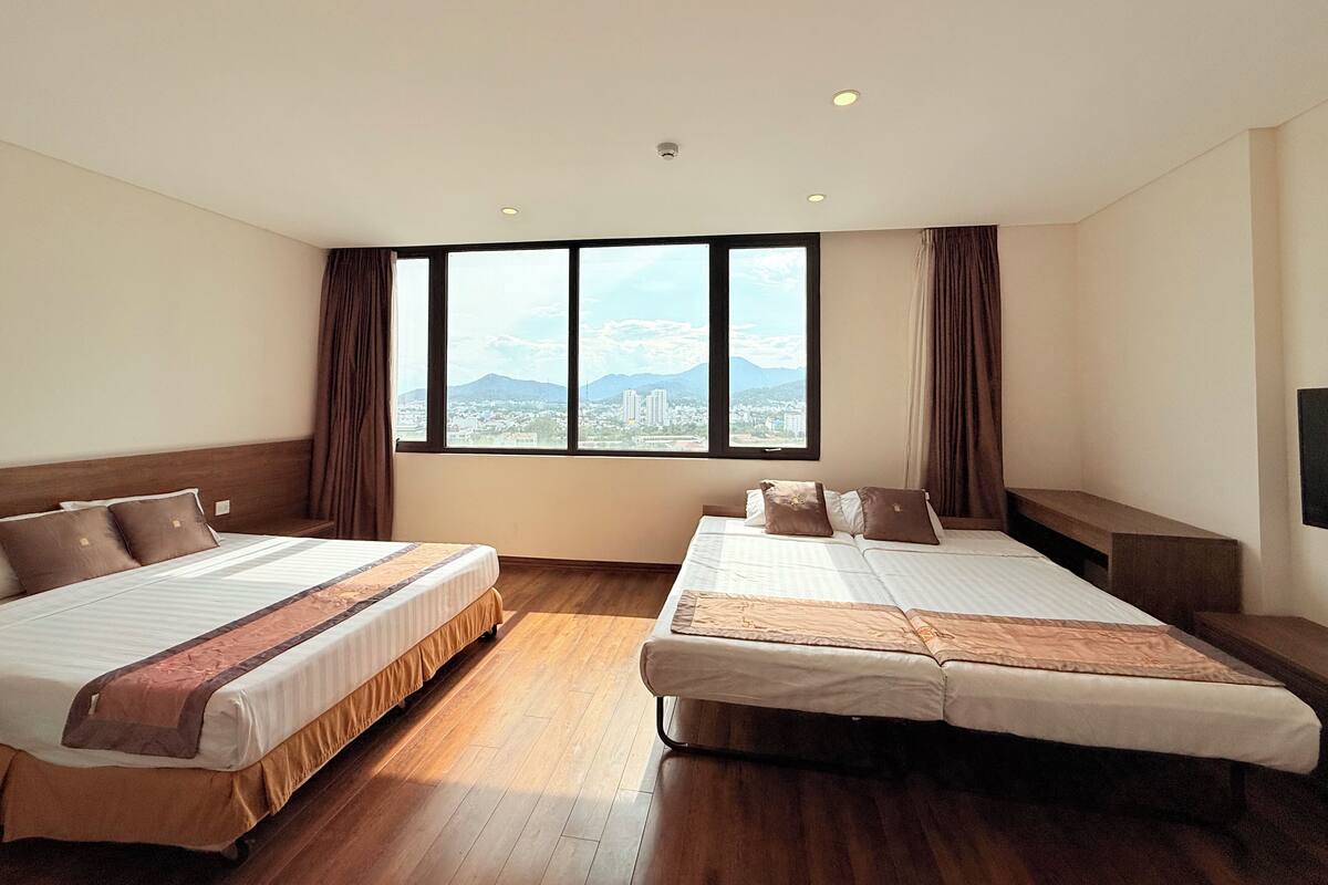 Een hotelkamer met twee bedden, een groot raam met uitzicht op de stad, houten vloeren en een flatscreen televisie aan de muur.