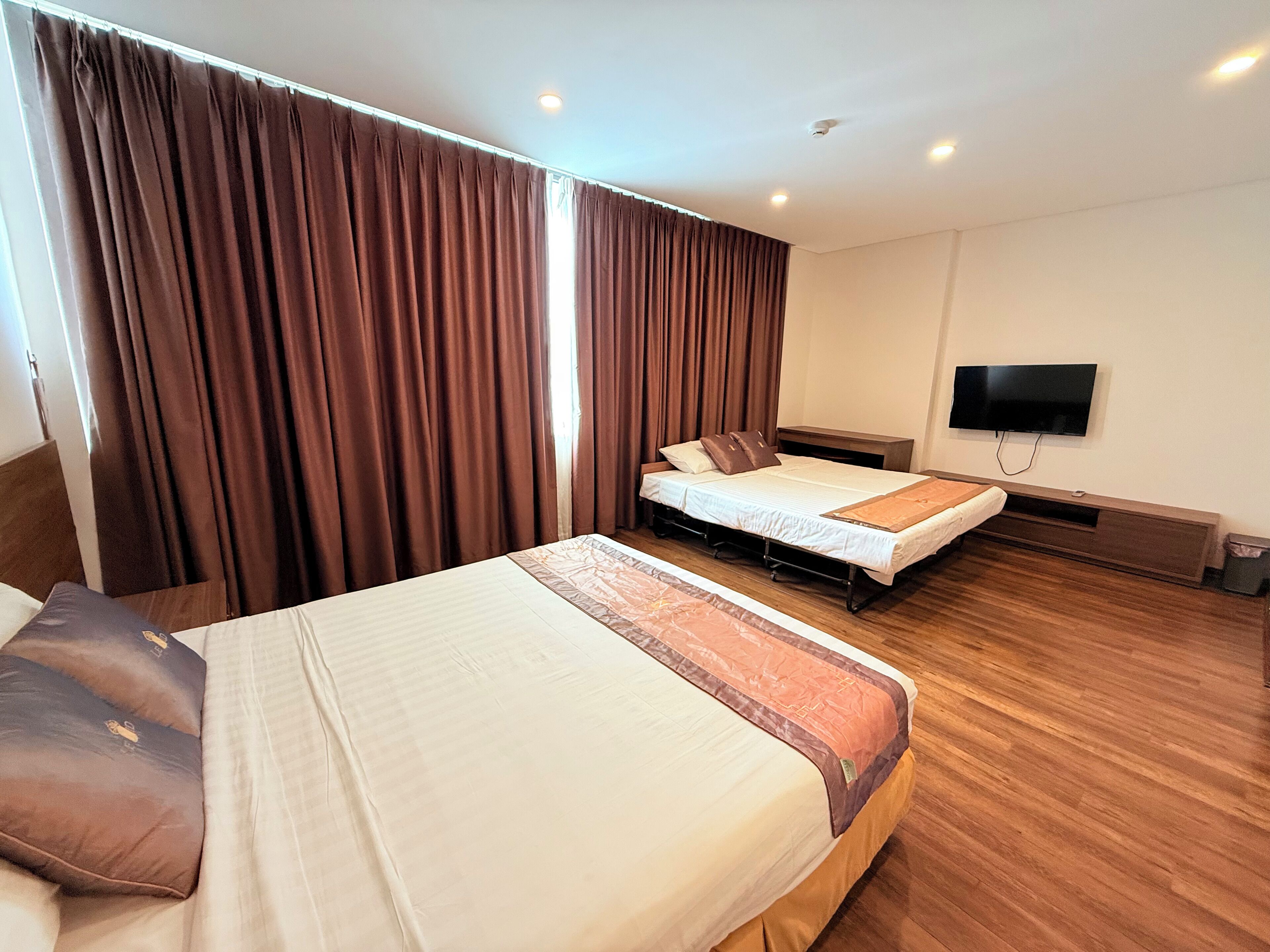 A hotel room with two beds, a TV, and a wooden floor.