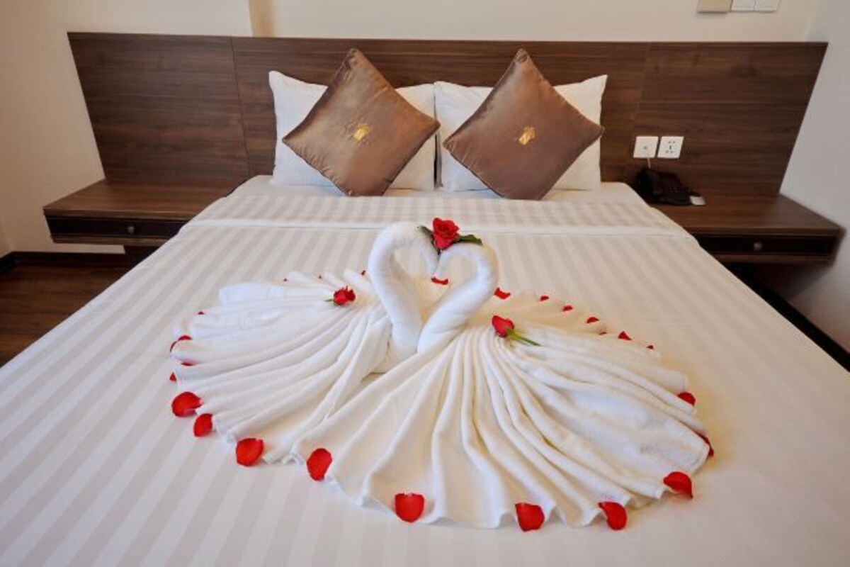 Un letto rifatto con cura, decorato con un cigno realizzato con asciugamani e petali di rosa.
