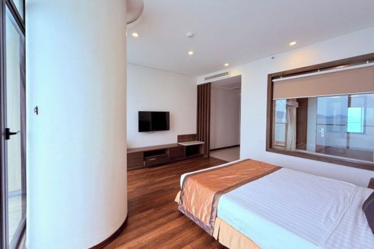 Una camera d'albergo moderna con un letto grande, una televisione a schermo piatto, un pavimento in legno e un'ampia finestra.