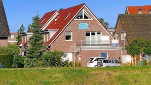 Ein zweigeschossiges Backsteinhaus mit rotem Dach, einem Schild und einem kleinen Parkplatz mit Autos.