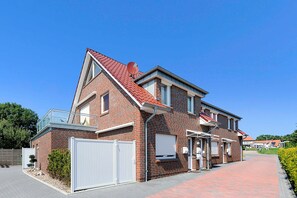 Et toetages murhus med rødt tegltag, en indgang med låge og et lille haveareal.