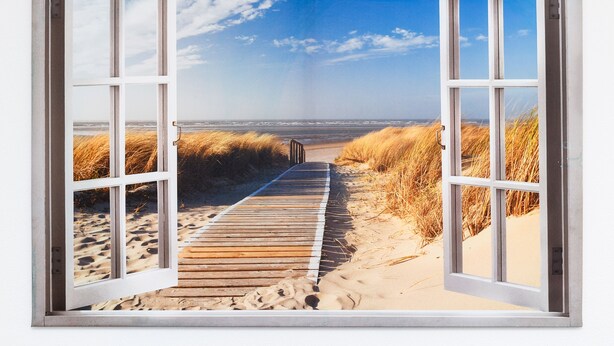 Ein offenes Fenster zeigt einen hölzernen Steg, der zu einem Strand mit Sand und Dünen führt.