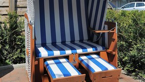 Ein Liegestuhl mit gestreifter Sitzauflage und Sonnendach, platziert auf einer Ziegelterrasse mit einem Gebäude im Hintergrund.