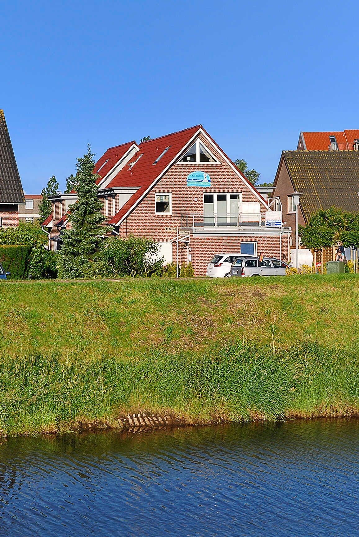 Un bâtiment en briques de deux étages, avec un toit rouge, une enseigne et un petit espace de stationnement où sont garées des voitures.