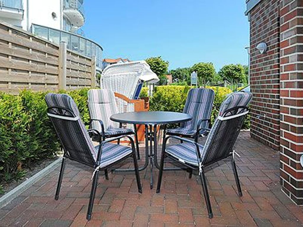 An outdoor patio with a round table and four chairs, surrounded by a brick wall and greenery.