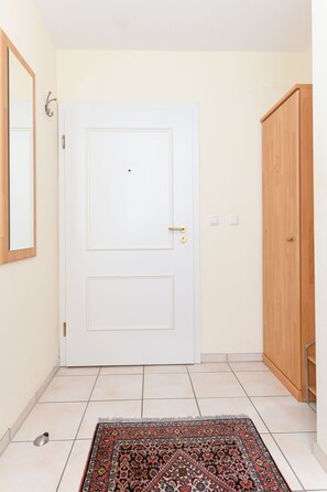 Eine weiße Tür mit goldener Klinke, ein Holzschrank und ein gemustertes Teppich auf Fliesenboden.