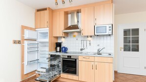 Kompakti keittiö, jossa on puukehikoiset kaapit, sisäänrakennettu mikroaaltouuni, astianpesukone ja liesi.