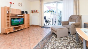 Olohuone, jossa on televisio, puinen mediakeskus, beigenvärinen sohva ja kuviollinen matto.