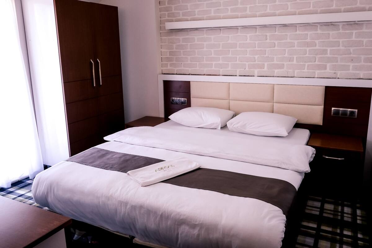 Een hotelkamer met een bed, een kledingkast, een nachtkastje en een muur met een baksteenmotief.