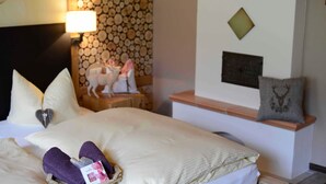 Camera d'albergo con un letto, cuscini, un comodino, una lampada, una parete con camino e uno scaffale con oggetti decorativi.