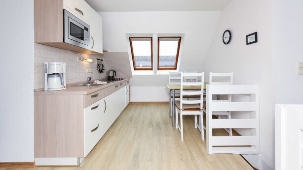 Moderni keittiö, jossa on mikroaaltouuni, kahvinkeitin sekä ruokailutila pöytineen ja tuoleineen.