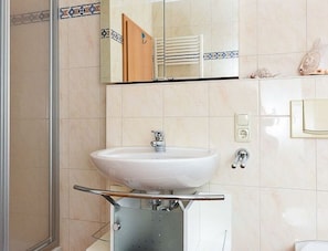 A bathroom with a white sink, a mirror above it, and a shower area.