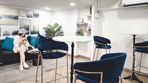 Un salon moderne avec un canapé, une table ronde et des chaises bleues. Des tableaux encadrés ornent le mur, et une plante en pot est posée dans un coin.