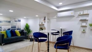 Un salon moderne avec un canapé, des fauteuils bleus, une table basse et un coin repas comprenant une petite table et des chaises.