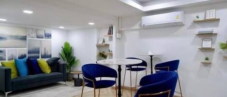 A modern living room with a sofa, blue chairs, a coffee table, and a dining area with a small table and chairs.