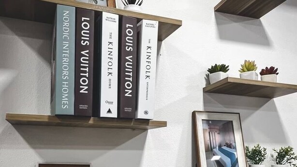 Un mur orné de plusieurs étagères en bois où sont exposés des livres, des photos encadrées et de petites plantes en pot.