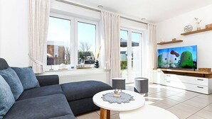 En moderne stue med sofa, rundt sofabord, fjernsyn og et vindue med gardiner.