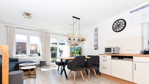 Et moderne køkken med hvide skabe, et spiseområde med bord og stole, og en opholdsstue med sofa og sofabord.