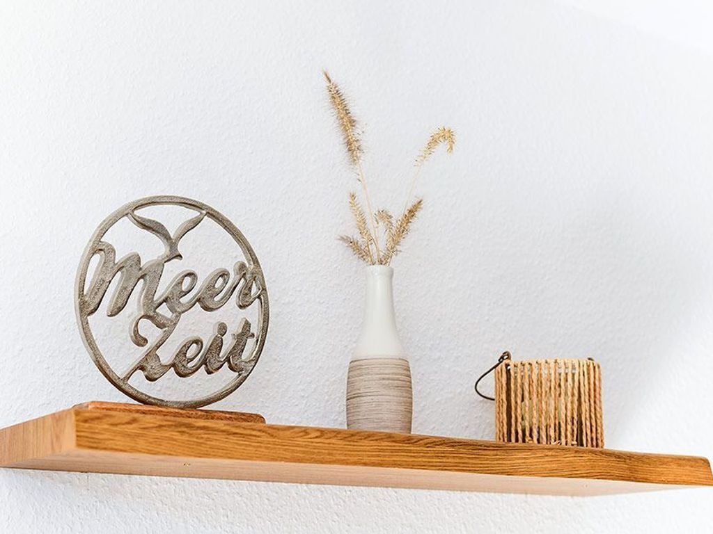 Une étagère en bois ornée d’une plaque métallique décorative, un vase blanc et un petit panier tressé.