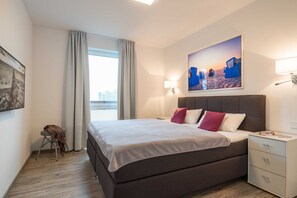 Une chambre d’hôtel moderne avec un grand lit, une table de chevet, une petite table avec une chaise et un tableau au mur.