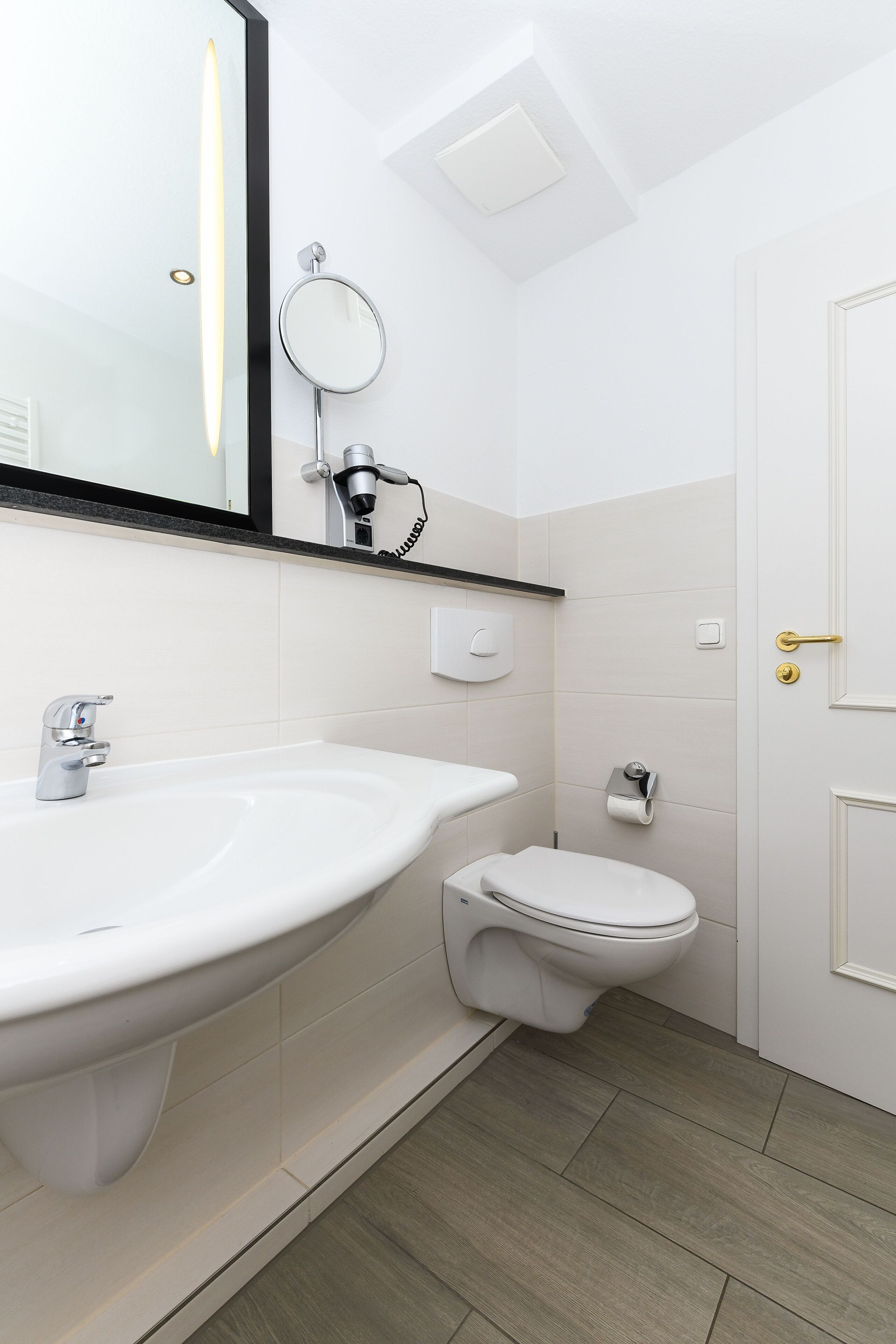 Une salle de bain moderne avec un lavabo blanc, des toilettes et un miroir au-dessus du lavabo.