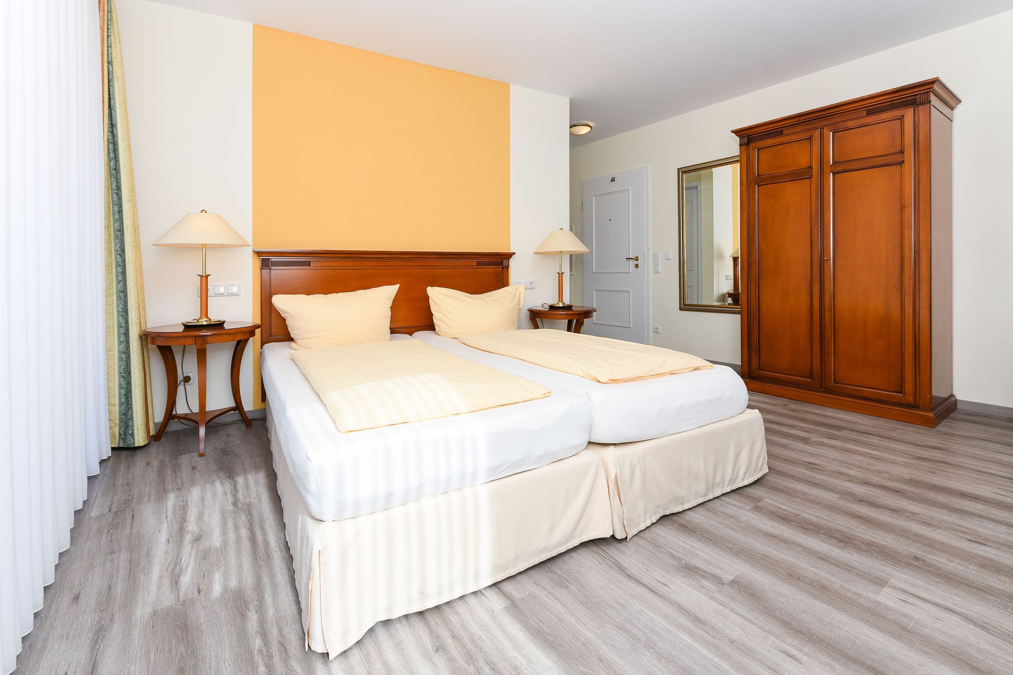 A hotel room with a double bed, two bedside tables with lamps, a wardrobe, and a mirror on the wall.