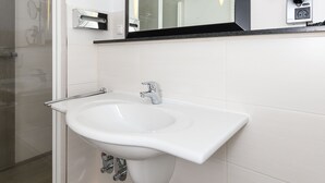 Une salle de bain moderne avec un lavabo blanc, un grand miroir et une douche à parois de verre.
