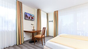 Une chambre d’hôtel avec un lit, un bureau, une chaise, une télévision et des rideaux.