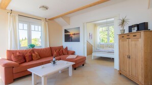 A living room with a sofa, a coffee table, a wooden cabinet, and a view through an open door. - Lighthouse - House Sun & Sea (Sierksdorf)